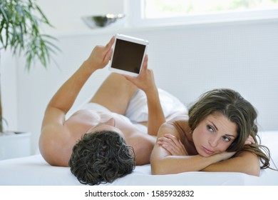 Bored Young Woman Next To Man Looking At Digital Tablet In Bed