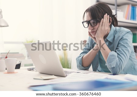 Bored young woman in the office working with a laptop and staring at computer screen