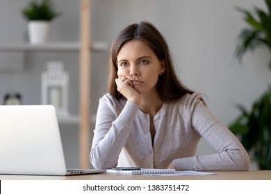Bored young woman sit at home office table look in distance unable to work at laptop, exhausted girl student feel unmotivated unwilling to study, distracted taking break. Dull monotonous job concept