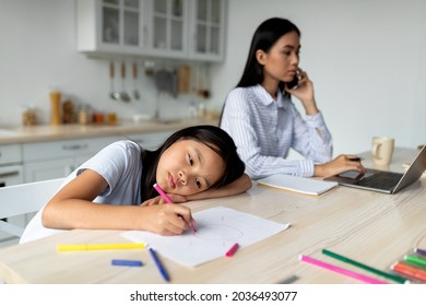 Boredom Concept. Busy Mom Working Remotely At Home And Ignoring Her Little Daughter, Kid Feeling Bored And Lonely, Drawing On Paper. Asian Mother And Daughter Sitting In Kitchen