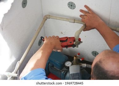 Borehole Water Pump Station Installation. A Man Is Connecting Water Supply Equipment, Water Pipes To A Water Pump In A Borehole Chamber. 