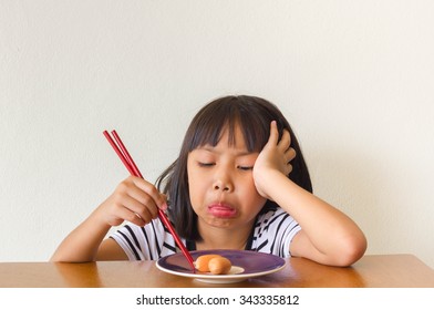 Boring asian children girl with food and red chopsticks sitting at the table