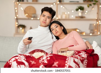 Boring Christmas. Bored Asian Family Couple Watching Movie On TV Holding Television Remote Control, Switching Channels Celebrating Christmas At Home. Social Distancing, Bad Xmas Eve And New Year