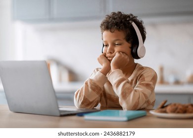 Boring Content. Upset little black boy in wireless headphones looking at laptop screen at home, bored african american preteen male child sitting at desk and using computer, copy space - Powered by Shutterstock