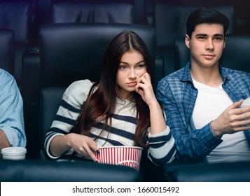 Boring Date Concept. Weary Young Girl With Boyfriend Watching Movie In Dark Cinema