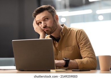 Boring Job. Unhappy Businessman Sitting Near Laptop Bored Of Computer Work, Thinking Of Problems In Modern Office. Business Issues And Entrepreneurship Difficulties Concept