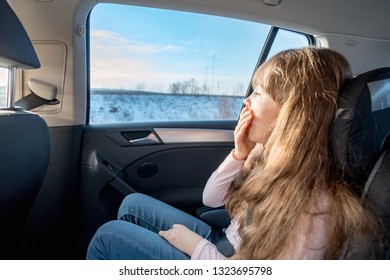 Boring Little Girl Sitting In Car Seat And Looking Through Window During Long Journey