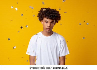 Boring Selebration. Party Failure. Unhappy Young African Male Standing In Confetti Rain Isolated On Orange Copy Space. Bad Surprise. Melancholic Mood