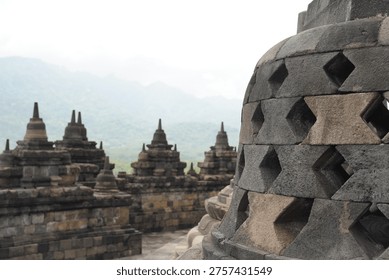 Borobudur, Central Java, Indonesia - July 12, 2024: Majestic stone stupas of the world’s largest Buddhist temple at sunrise. Ancient UNESCO heritage site showcasing intricate reliefs and statues.