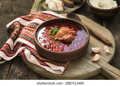 Borscht - Traditional Ukrainian dish.  Vegetable soup made from beets, potatoes, cereals and boiled meat, and  slices of rye bread in a ceramic bowl on a wooden kitchen table. Russian  food cuisine - Shutterstock ID 2087511400