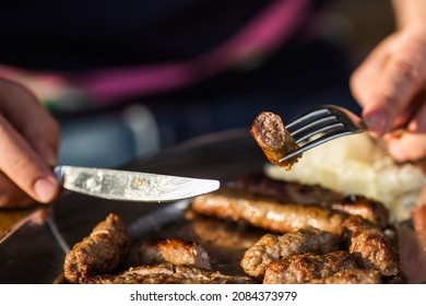 Bosnian traditional minced meat dish called Cevapi and Pljeskavica, cut out with knife and fork  outdoors in a restaurant called Cevabdzinica