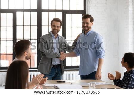 Boss shake hands introduces new employee to members during briefing in board room, staff clap hands encourage newcomer welcoming express regard. Praise and appreciation, best worker of month concept