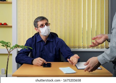 Boss Sits At A Table In The Office And, In A Conversation With An Employee, Invites Him First Of All To Take A Medical Face Mask. Using Safety Measures, People Continue To Work