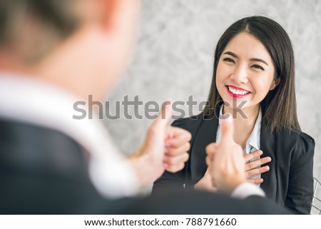 Boss/Business man employer admires young Asian business woman/staff/employee by thumb up and clap with smiling face for her success and good/best in work and recognition/appreciate.
