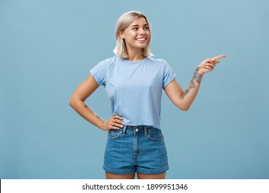 Bossy Confident Female Manager With Tattoo On Arm Holding Hand On Waist Pointing And Gazing Right With Pleased Relaxed Look Giving Directions To Employees Posing Over Blue Background