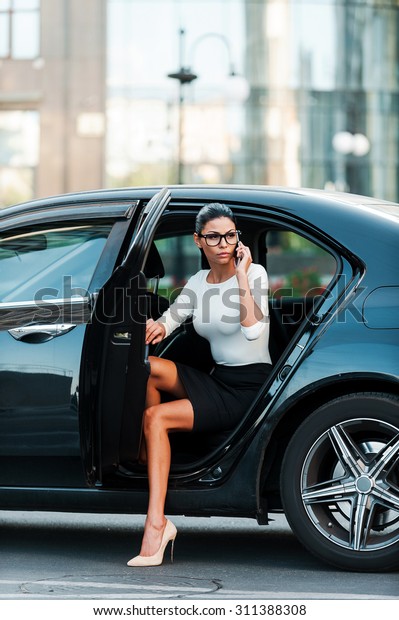 Bossy woman. Confident young\
businesswoman talking on the mobile phone while coming out her\
car