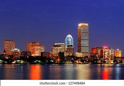 Boston city skyline at dusk with Prudential Tower and urban skyscrapers over Charles River with lights and reflections.