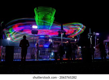 Boston,  Lincolnshire, England- October 24, 2021. Carousel motion lights in the  Central Park and Skatepark fair with people standing and looking at the carousel. Long exposure photography.