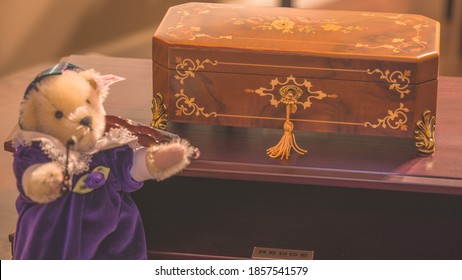 Boston, MA, USA 11/16/2020 — Closed Reuge Inlay Wood Music Box On Its Accompanying Amplifier Soundboard. Steiff “Muffy Musical Soiree” Teddy Bear Playing The Violin To The Front Of The Photo In Bokeh.