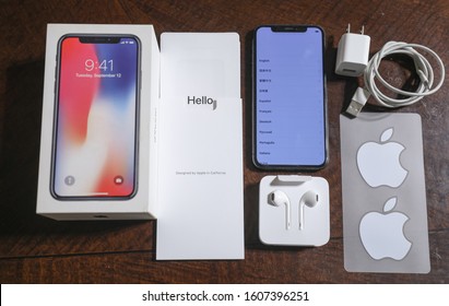 Boston, MA, USA 12/28/2019 — Apple’s 64 MB iPhone X with its original box and accessories in flat lay on a mahogany wood table.
