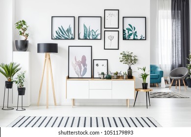 Botanical posters on the wall in a living room interior with white cabinet, wooden lamp and plants