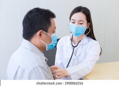Both of Asian woman doctor and a man patient wear medical face mask to protect infectious disease (Covid 19) while check up health in hospital.  - Shutterstock ID 1900062316