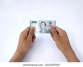 Both hands holding a two thousand rupiah (2000) . Isolated on a white background.


