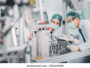 Both male and female Asian scientists are outfitted with protective gear. Examining the factory's machinery and materials used in the mask-making process. Covid 19 is a piece of preventive equipment. - Powered by Shutterstock