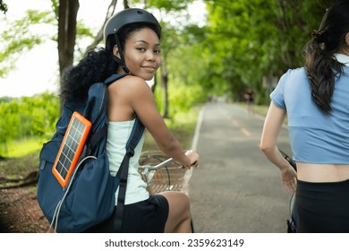 Both of young women in sportswear riding a bicycle in the park, Carry a backpack with a solar panel to charge smartphone. - Powered by Shutterstock