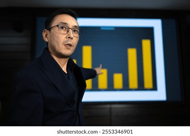 Bothered marketer in formal attire is presenting statistical data during business meeting gesturing towards colorful bar chart displayed on the large screen behind him, indicating important points. - Powered by Shutterstock