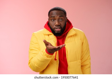 Bothered rude ignorant african-american bearded man pointing palm camera look dumb perplexed, standing confused cannot get clue what happening, wearing yellow jacket, pink background