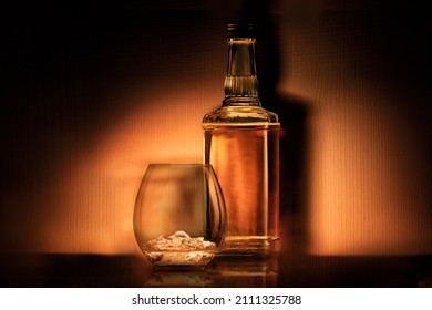 A Bottle Of Alcohol Rum Whiskey Or Bourbon And A Glass With Ice On A Dark Orange Background, Retro Still Life