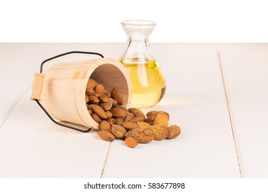 Bottle of almond oil and almonds on white wooden background