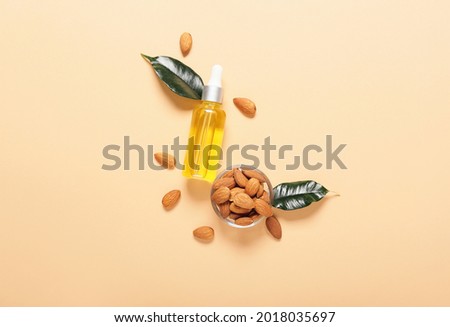 Bottle of almond oil and nuts on color background