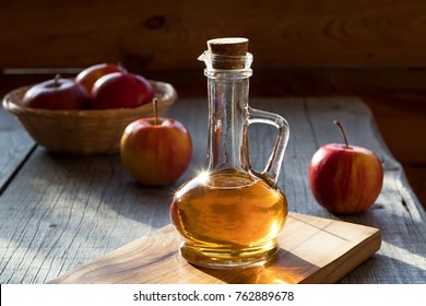 A bottle of apple cider vinegar in the morning sun, with apples in the background