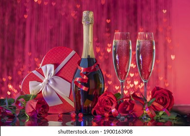 Bottle and beautiful glasses with sparkling wine, luxurious gift box in the shape of a heart with a satin bow surrounded by selected roses on a mirror surface on a red shining bokeh background - Powered by Shutterstock