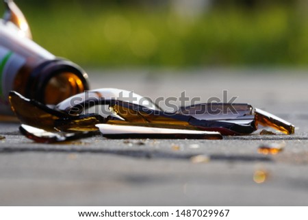 bottle of beer, soda or drugs from dark glass is broken. Shattered beer bottle on ground in sunset light. Fragments of glass on asphalt. Texture, background, wallpaper.