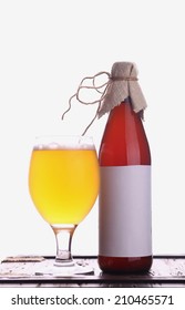 Bottle With Blank Label Template And Glass Of Home Brewed Craft Beer Standing On A Wooden Chest With Bright White Background