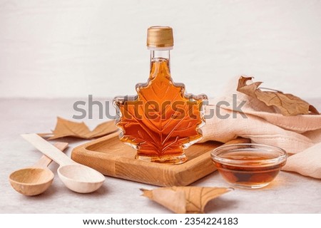 Bottle and bowl of tasty maple syrup on light background