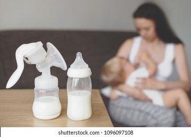Bottle and breast pump with breast milk on the background of mother holding in her hands and breastfeeding baby. Maternity and baby care.