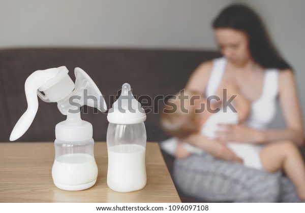 Bottle and breast pump with breast milk on the\
background of mother holding in her hands and breastfeeding baby.\
Maternity and baby care.