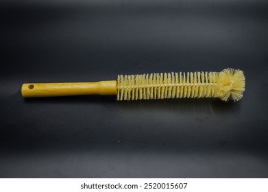 A bottle brush with a wooden handle and yellow bristles on a black background - Powered by Shutterstock