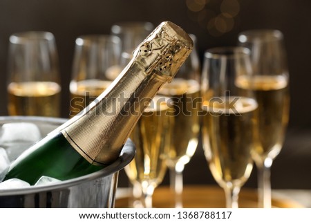 Bottle of champagne in bucket with ice and glasses on blurred background, closeup. Space for text