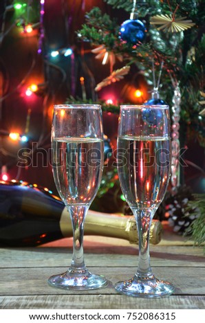 a bottle of champagne and glasses on the background of a Christmas tree decorated with balls and New Year's lights. happy christmas concept. Ribbon, baubles and wine against Christmas lights