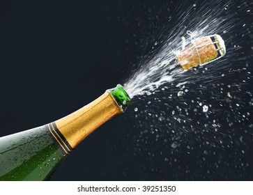 Bottle Of Champagne With Popping Cork And Champagne Spray On Black Background.