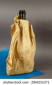 Bottle Of Champagne Without Cork In Paper Bag On Blue-gray Background. Dark Bottle Of Alcohol In A Crumpled Brown Bag. Close-up. Selective Focus.