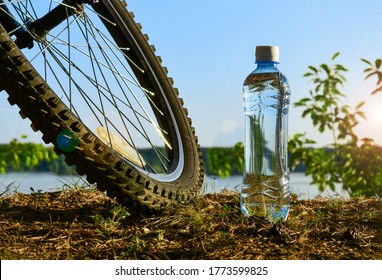 A bottle of clean water and a Bicycle wheel on the background of the lake shore. Rest after exercise on a summer evening.