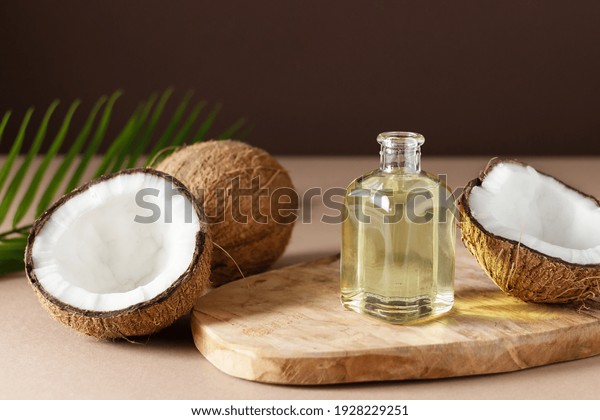 Bottle\
of coconut oil and fresh coconuts with palm leaf on wooden board\
over brown background. Coconut natural\
cosmetics.