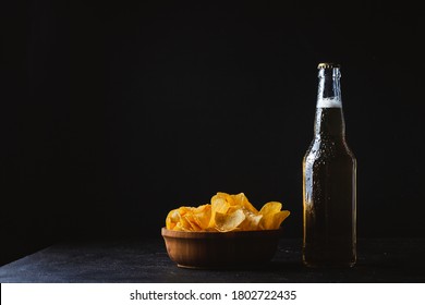 A bottle of cold beer next to crunchy potato chips in the wooden bowl on the dark background
 - Powered by Shutterstock