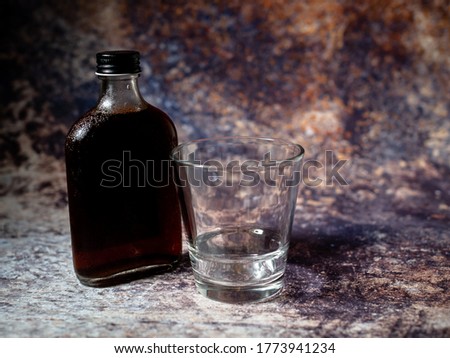 A bottle of cold brew coffee and empty glass against rusty background 